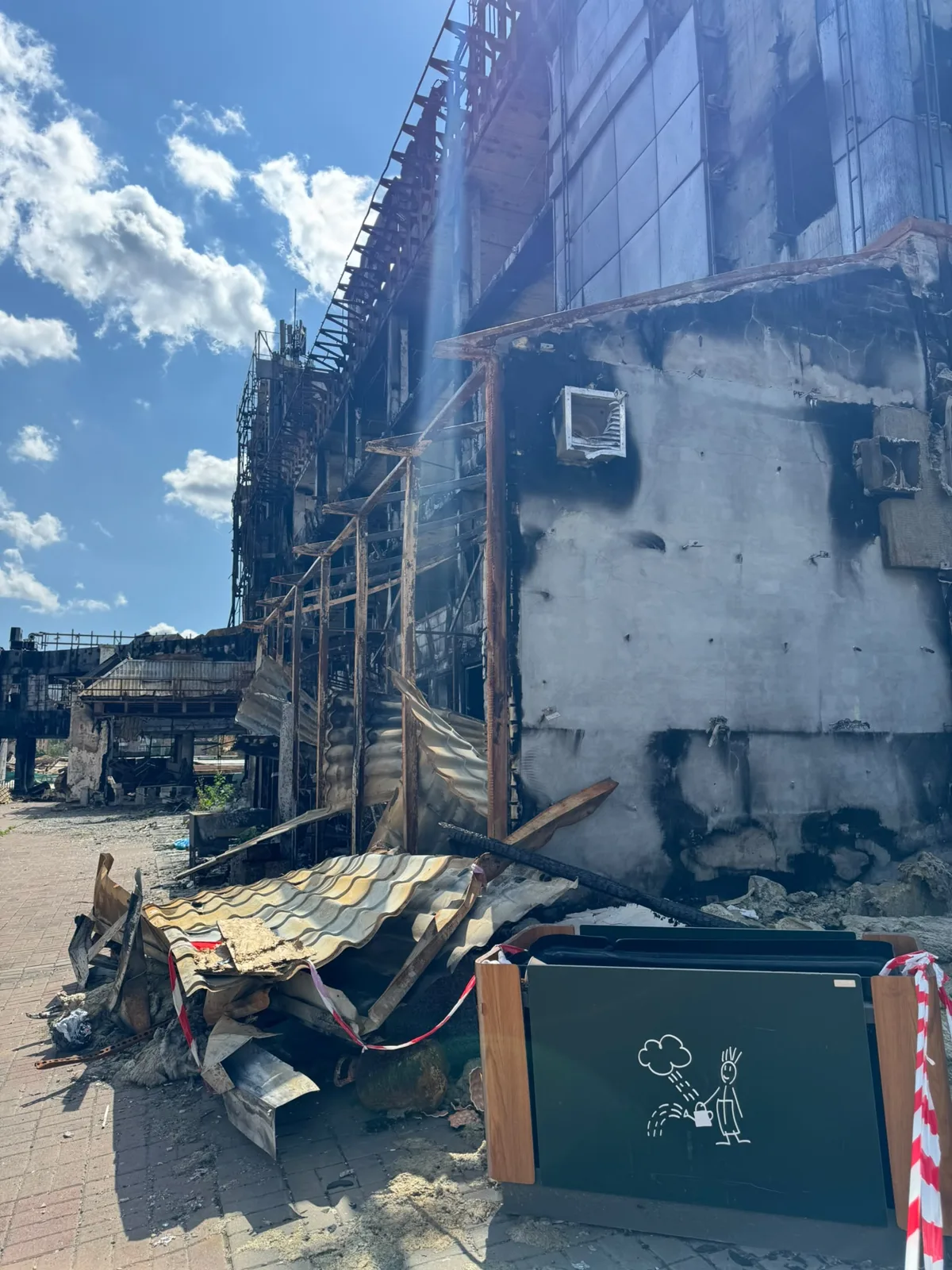 Ausgebrannte Fassade eines Einkaufszentrums mit Trümmern und Absperrband